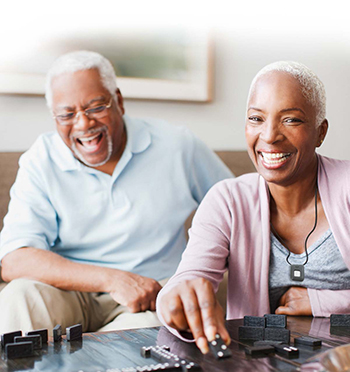 Senior couple wearing medical alert necklace playing dominos